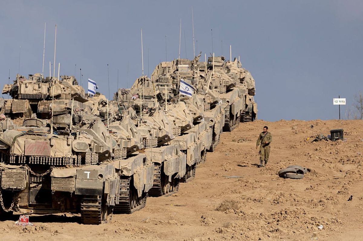 An Israeli soldier walks near tanks as they are stationed near the border with the Gaza Strip