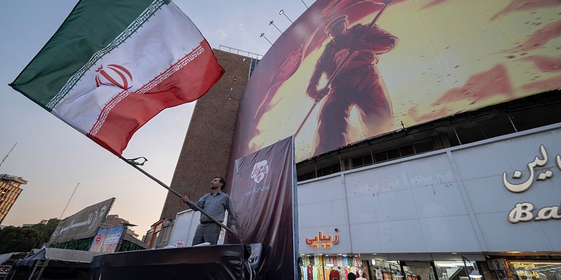 Daily Life In Tehran As Iran-U.S. 60-day Ceasefire Expires A pro-government supporter waves an Iranian national flag from a stage set up along a street in downtown Tehran, Iran, on August 23, 2026, following the expiration of the 60-day ceasefire between Iran and the United States on August 17. (Photo by Morteza Nikoubazl/NurPhoto via Getty Images)