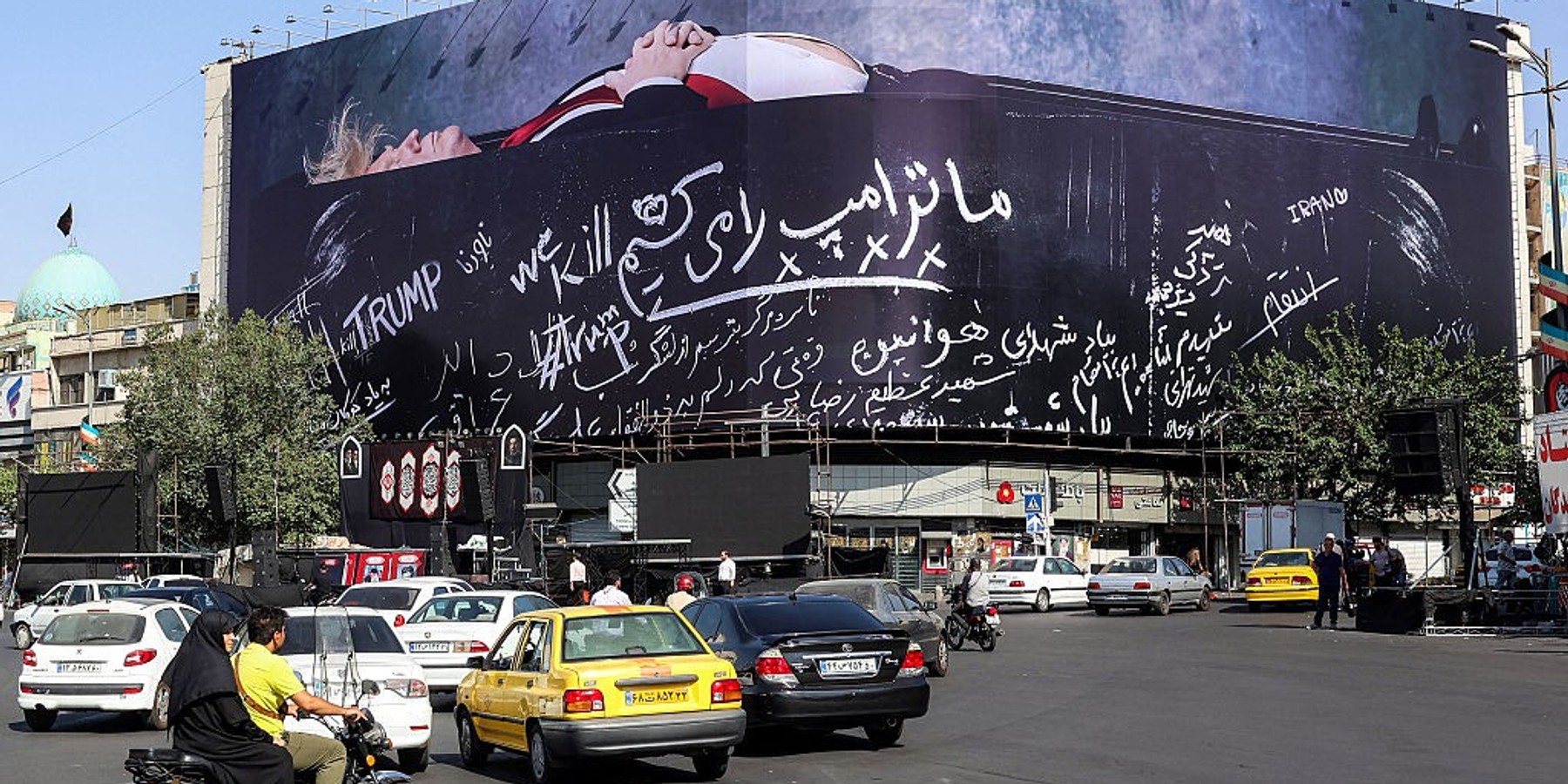 IRAN-US-ISRAEL-WAR Motorists drive along Tehran's Enghelab Square on July 15, 2026, past a giant anti-US billboard featuring US president Donald Trump in a coffin with text in Persian reading "We Kill Trump". Hostilities renewed between Iran and the US, endangering a memorandum of understanding, reached in June with Qatari and Pakistani mediation, aimed at ending the war. The confrontation resumed on July 7 after attacks on ships in the Gulf, which Iran has attributed to Iran. (Photo by AFP via Getty Images) /