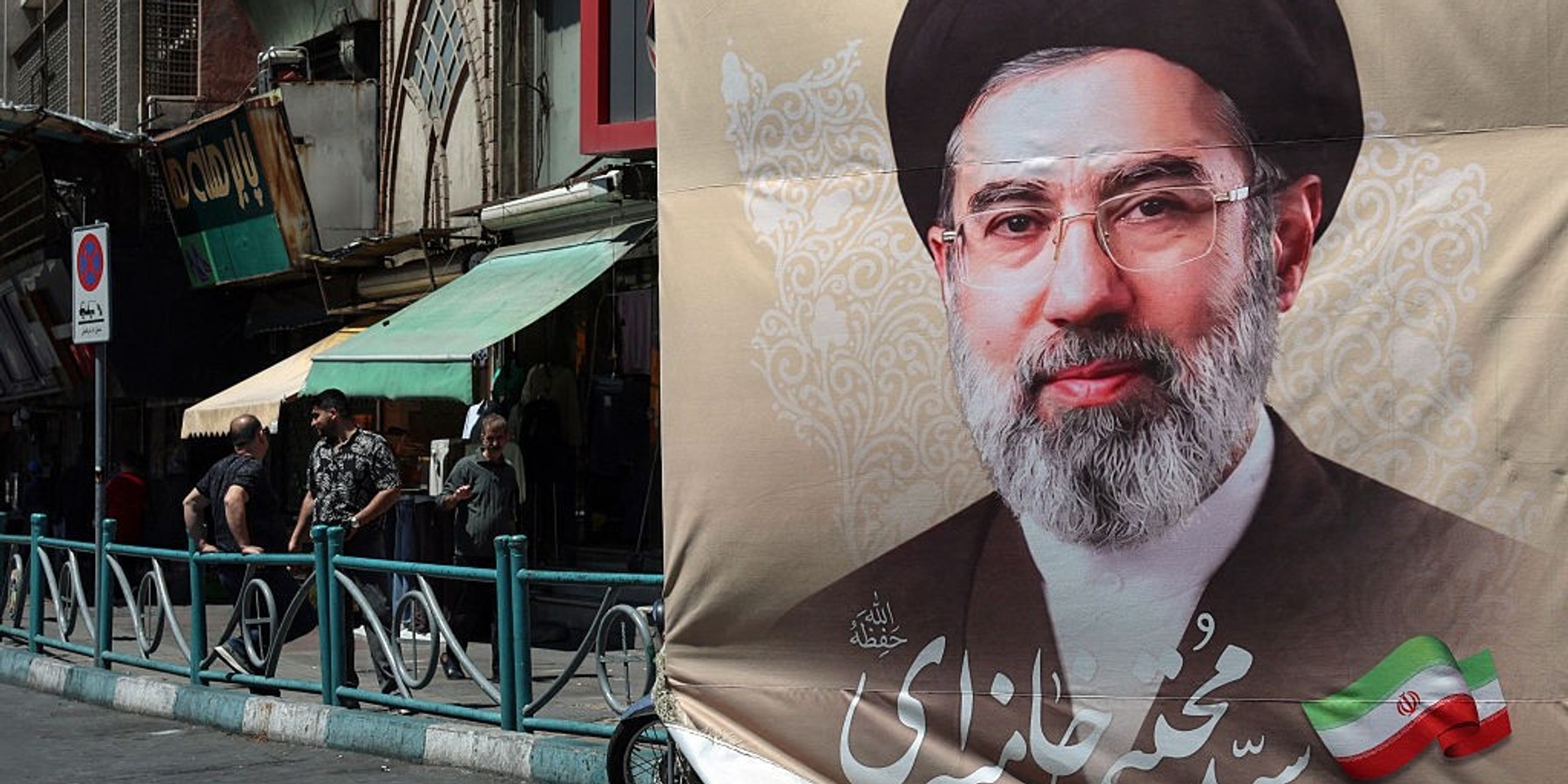 Iranians stand on a pavement along a street next to a billboard depicting Iran's Supreme Leader Ayatollah Mojtaba Khamenei, in Tehran on April 24, 2026. (Photo by AFP via Getty Images) /