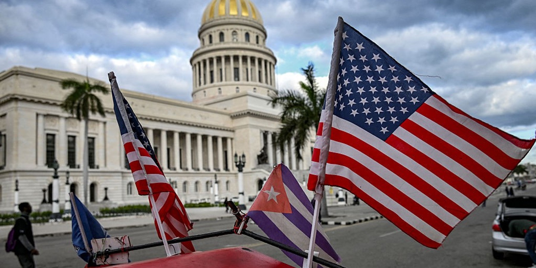 TOPSHOT - Two US flags and a Cuban flag flutter on the roof of a tricycle in front of the Capitolio in Havana on February 3, 2026. Cuba's government on February 2 told AFP that it was in "communication" with US President Donald Trump's administration but not yet in formal talks on a deal to end Washington's pressure campaign on the island. (Photo by YAMIL LAGE / AFP via Getty Images)