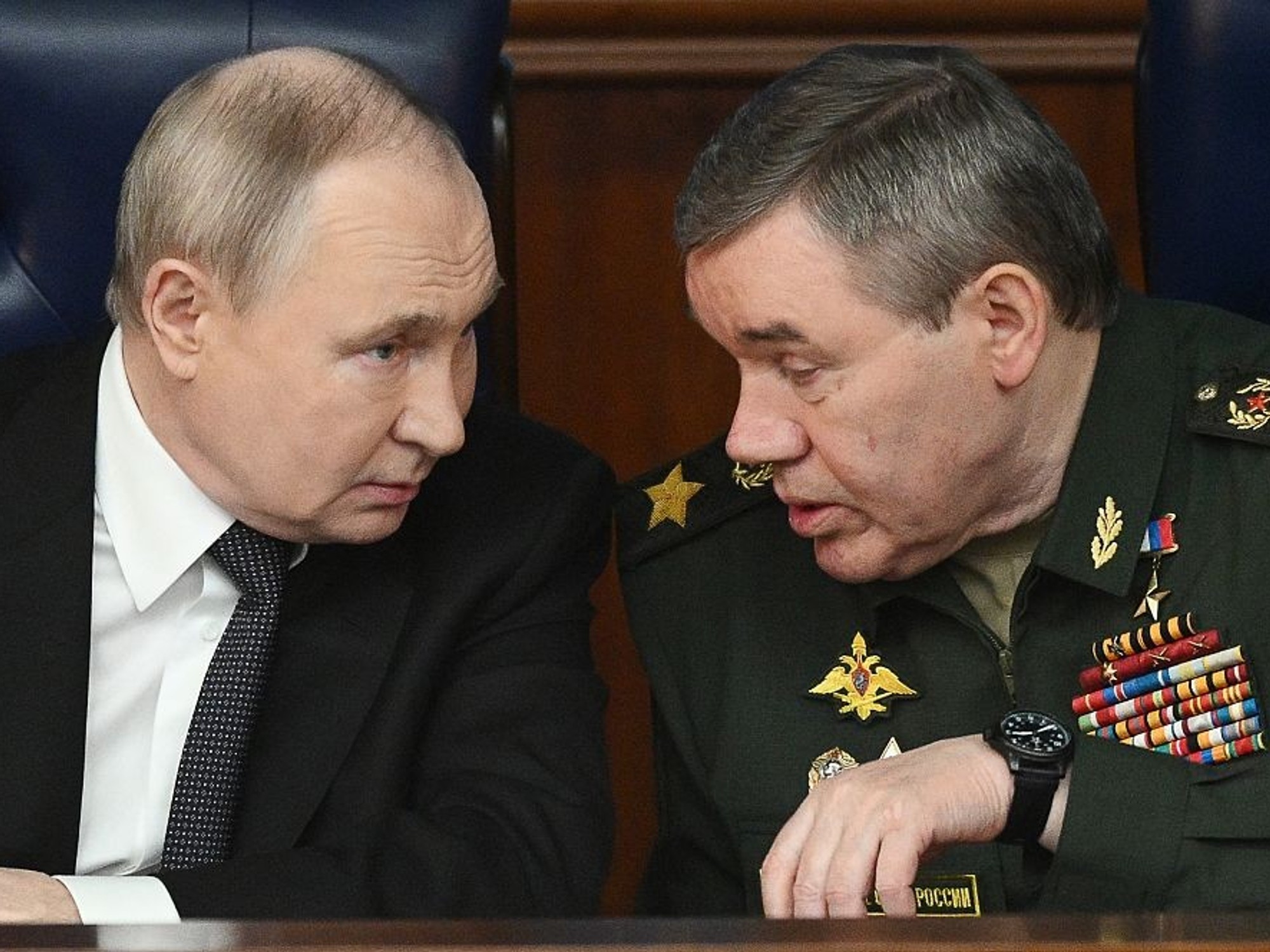 Two men in a serious conversation, one in a suit, the other in a military uniform.
