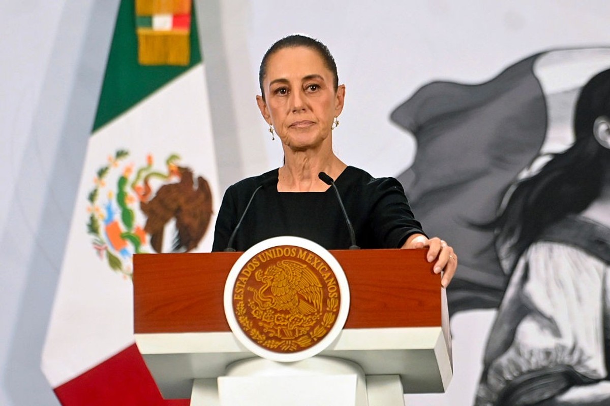 Woman speaking at podium with Mexican seal, flag, and artwork in background.